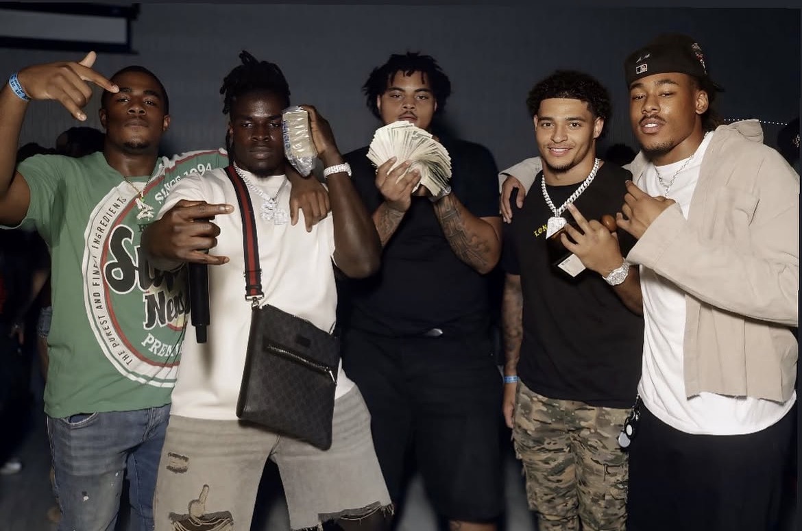 Five friends posing together at a night function, money fanned to the camera