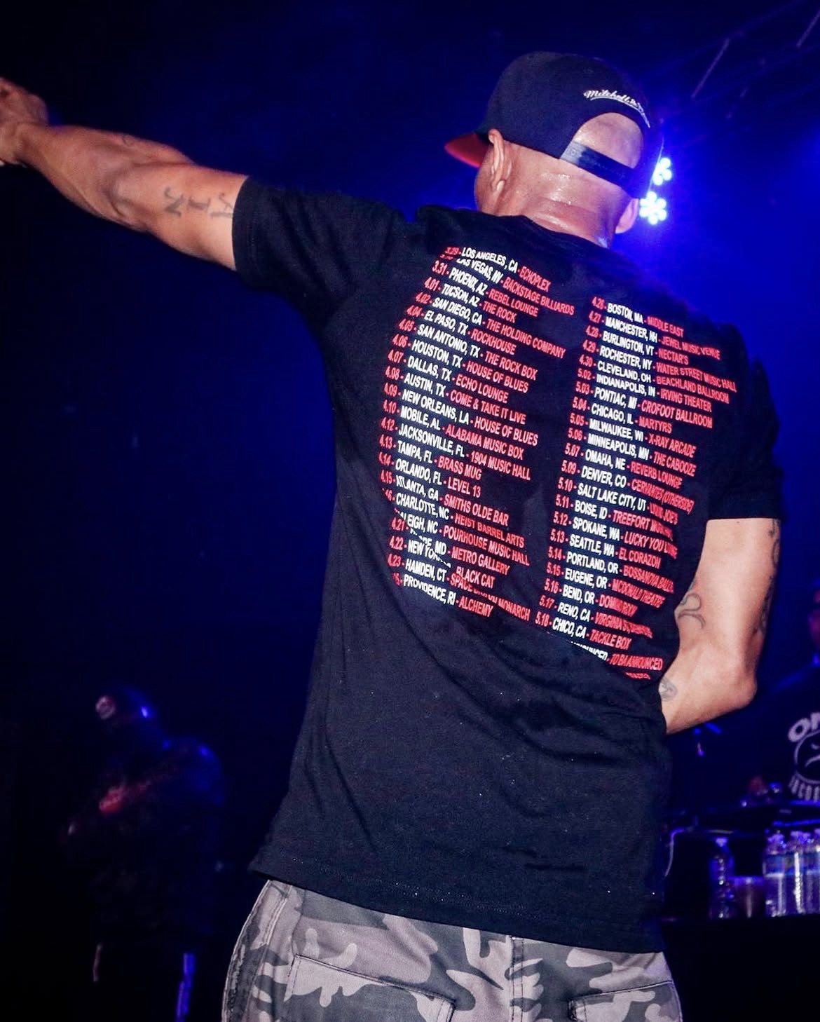 Performer on stage in blue light with tour dates across his shirt